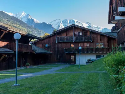 a group of wooden buildings with mountains in the background at Ski-in/ski-out & pool: great for summer and winter in Saint-Gervais-les-Bains