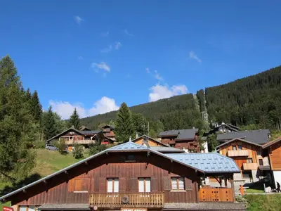 a group of wooden buildings with a mountain in the background at 3 pièces pour 6 personnes face aux pistes et commerces, stationnement inclus - FR-1-572-190 in Arâches-la-Frasse