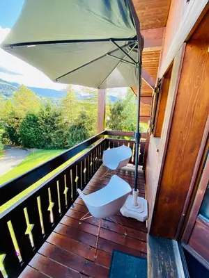 a porch with two white chairs and an umbrella at Appartement face Mont Blanc in Demi-Quartier