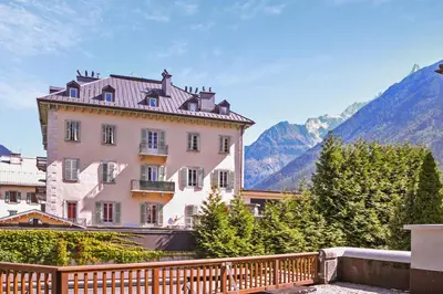 a large pink building with a wooden fence in front of mountains at Appartement Lyret - Welkeys in Chamonix-Mont-Blanc