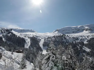 a snow covered mountain with trees and the sun in the sky at Studio rénové à Flaine Forêt - 5 pers, proche des pistes et commerces, balcon sud, casier à skis - FR-1-687-24 in Arâches-la-Frasse
