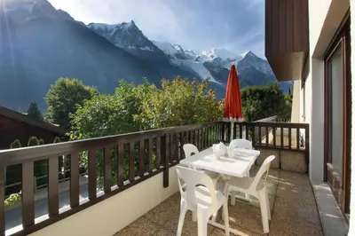 a table and chairs on a balcony with a view of mountains at Les Terrasses de Planpraz - 8min Walk to Center - Quiet - Perfect for Hiking in Chamonix-Mont-Blanc