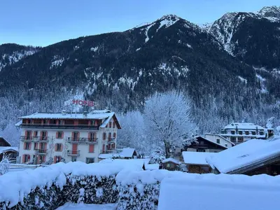 a building covered in snow with mountains in the background at L'écrin des Bossons in Chamonix-Mont-Blanc