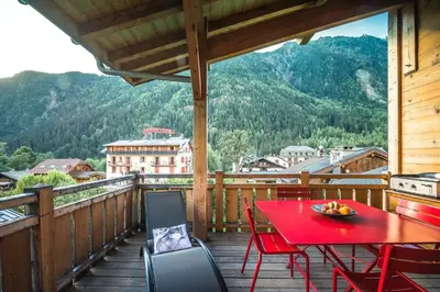 a red table and chairs on a balcony with a view at L'écrin des Bossons in Chamonix-Mont-Blanc