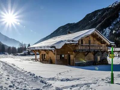 a log cabin in the snow with the sun behind it at Magnifique chalet 12 pers avec sauna et cheminée - FR-1-343-181 in Chamonix-Mont-Blanc