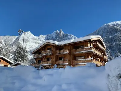 a building covered in snow with mountains in the background at Bel appartement 3 étoiles aux Praz de Chamonix, près du téléphérique de la Flégère - FR-1-343-213 in Chamonix-Mont-Blanc