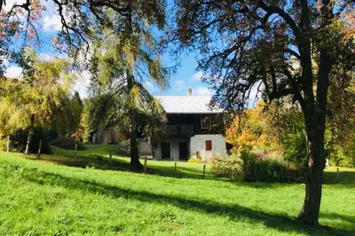 a house on a green field with trees in the foreground at Le Chalet de Bémont in Samoëns