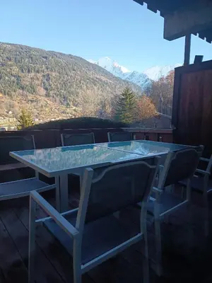 a glass table and chairs on a balcony with mountains at Saint-Gervais, appart cosy, piscine & pied des pistes in Saint-Gervais-les-Bains