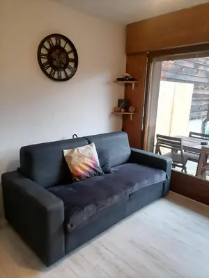 a blue couch in a living room with a clock on the wall at Saint-Gervais, appart cosy, piscine & pied des pistes in Saint-Gervais-les-Bains