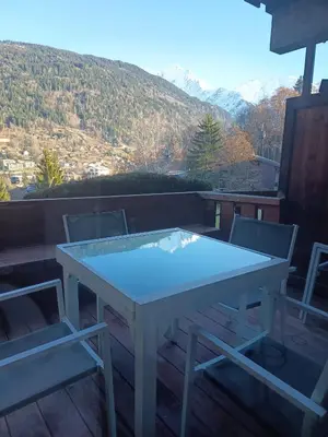 a white table and two chairs on a deck with mountains at Saint-Gervais, appart cosy, piscine & pied des pistes in Saint-Gervais-les-Bains