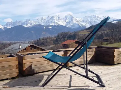 a blue chair sitting on top of a deck with mountains at Chalet à Cordon face à la chaîne du Mont Blanc in Cordon