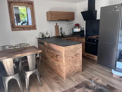 a kitchen with a counter and a table and a refrigerator at Logement avec jardin et vue panoramique MontBlanc in Les Houches