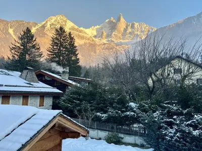 a snow covered house with mountains in the background at Le Chaney - T2 dans chalet - Massif du Mont-Blanc in Chamonix-Mont-Blanc