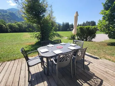 a table with chairs and an umbrella on a wooden deck at Cascades, 3 bedroom chalet with shared pool. in Samoëns