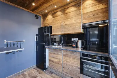 a kitchen with wooden cabinets and a black refrigerator at Le Nid d'Aigle - Modern Apartment Next to Ski lift Prarion - By Cozee Rentals in Les Houches