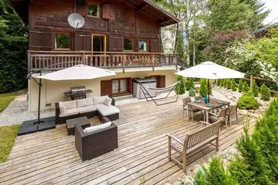 a wooden deck with furniture and umbrellas in front of a house at Chalet des Favrands in Chamonix-Mont-Blanc