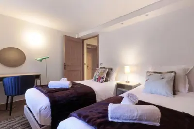 a hotel room with two beds and a chair at Les Alpins - Centre de Chamonix - Rénové avec Jardin et vue imprenable sur le MontBlanc in Chamonix-Mont-Blanc