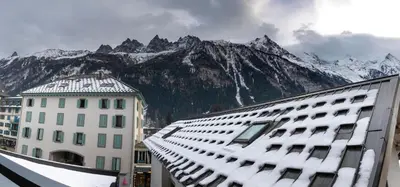 a building with snow on it and mountains in the background at L'Outa - Center of Chamonix - Mont-Blanc view in Chamonix-Mont-Blanc