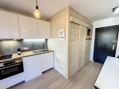 a kitchen with white cabinets and a wooden wall at Superbe studio refait à neuf et tout équipé avec parking in Chamonix-Mont-Blanc