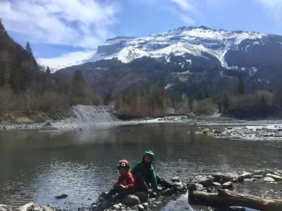 two people sitting on rocks in a river with a mountain at Gîte Ferme Sixt-Fer-à-Cheval in Sixt