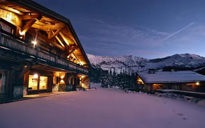 a building with snow on the ground next to a mountain at Rock and Stars Megève in Megève