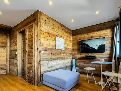a room with a wooden wall with a tv and a stool at Pti bout villlage Megeve in Megève