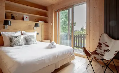 a bedroom with a bed and a chair and a window at Luxury Wood Megeve village in Megève