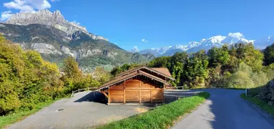 a wooden cabin on a road with mountains in the background at SUPERBE DEMI CHALET LUXUEUX 120M² 8 Personnes à SALLANCHES. in Sallanches