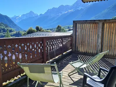 a deck with chairs and mountains in the background at Appartement Bellevue Au pied des pistes in Les Houches
