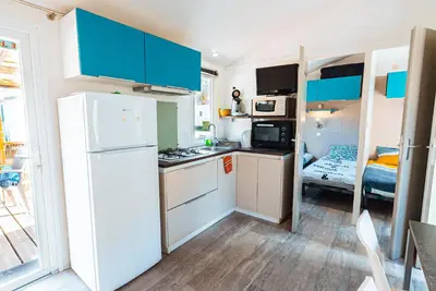 a small kitchen with a white refrigerator and a bedroom at Bungalow 3 chambres pour 6 pers avec Climatisation Camping 3 etoiles in Samoëns